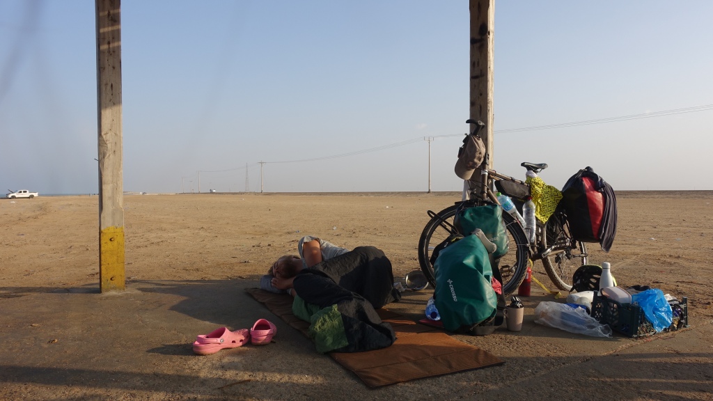 A traveller sleeping on a floor mat besides a bicycle loaded with front paneers.